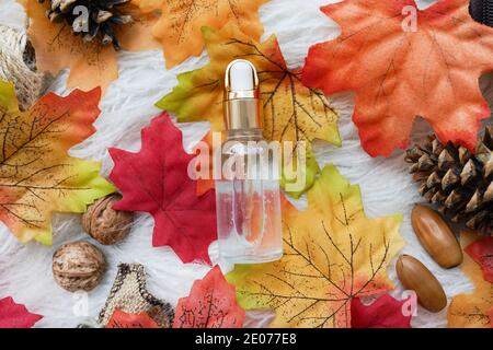Concetto biologico naturale di cosmetici autunnali. Bottiglie cosmetiche di olio essenziale su fondo bianco con coni e foglie gialle Foto Stock