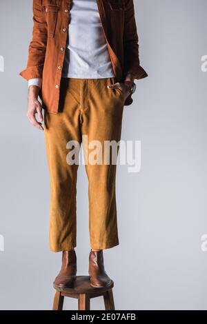 Vista dal taglio corto di un uomo elegante con mano in tasca su sedia isolata in grigio Foto Stock