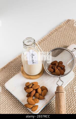 Latte di mandorle etichettato in una bottiglia accanto ad un filtro pieno di mandorle e un mazzo di loro. Vista verticale. Foto Stock