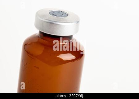Una macro shot con fuoco selettivo di un flacone di iniezione di vaccino color ambra su uno sfondo bianco chiaro. Foto Stock