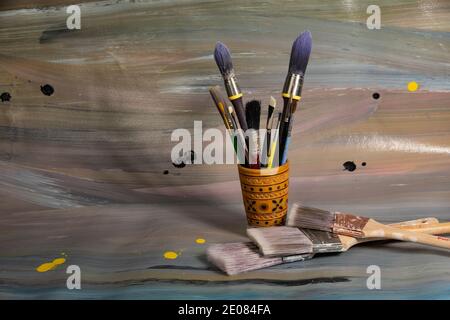 Spazzole per la pittura in una cassa di legno a matita su cui giace una vecchia tela dipinta con vernici ad olio Foto Stock