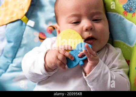 Concetti di infanzia, felicità, maternità - infantile sorpreso, divertente neonato bambino di età 3-4 mesi giocando con giocattoli, stuzzicadenti gnawing su Foto Stock