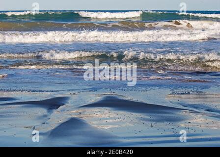 Il mare può creare alcuni effetti piuttosto interessanti - scorrendo sulla spiaggia di sabbia e disperdendosi sui canali formati. Foto Stock