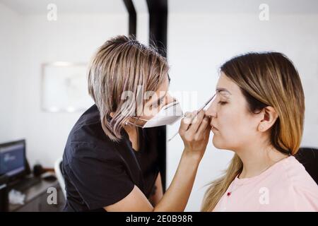 Cosmetologa latina che si prepara alla donna messicana per la procedura di trucco permanente sopracciglia in Messico, closeup Microblading Foto Stock