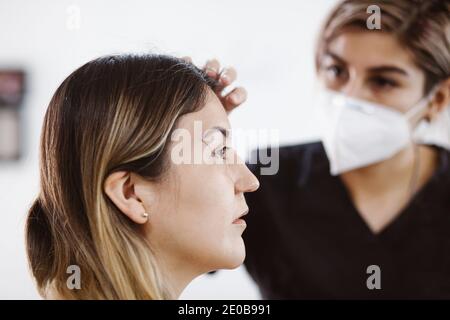 Cosmetologa latina che si prepara alla donna messicana per la procedura di trucco permanente sopracciglia in Messico, closeup Microblading Foto Stock