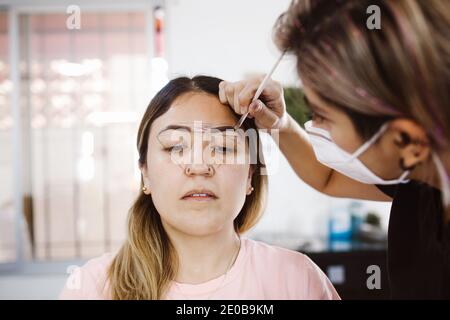 Cosmetologa latina che si prepara alla donna messicana per la procedura di trucco permanente sopracciglia in Messico, closeup Microblading Foto Stock