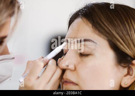 Cosmetologa latina che si prepara alla donna messicana per la procedura di trucco permanente sopracciglia in Messico, closeup Microblading Foto Stock