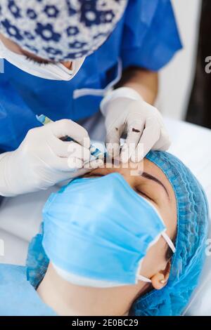 Cosmetologa latina che si prepara alla donna messicana per la procedura di trucco permanente sopracciglia in Messico, closeup Microblading Foto Stock