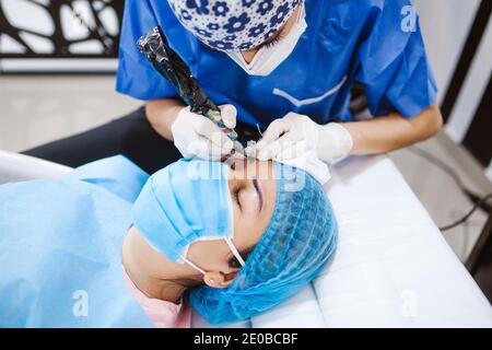 Cosmetologa latina che si prepara alla donna messicana per la procedura di trucco permanente sopracciglia in Messico, closeup Microblading Foto Stock