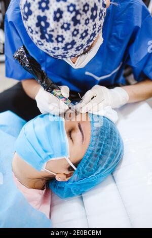 Cosmetologa latina che si prepara alla donna messicana per la procedura di trucco permanente sopracciglia in Messico, closeup Microblading Foto Stock