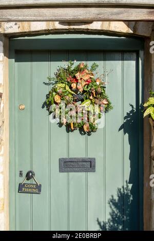 Ghirlanda di Natale su un cottage porta in Lower Slaughter. Cotswolds, Gloucestershire, Inghilterra Foto Stock