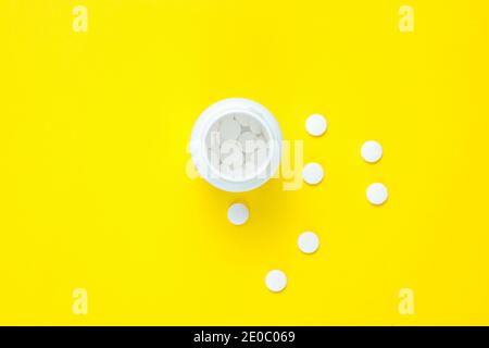 Concetto medico minimalista. Flacone aperto con pillole bianche su sfondo giallo pastello. Vista dall'alto Foto Stock