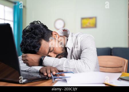 Il giovane si è stancato di lavorare e ha dormito sulla scrivania - esausto millennial si addormenta dopo aver letto sul laptop - concetto di napping sul luogo di lavoro Foto Stock