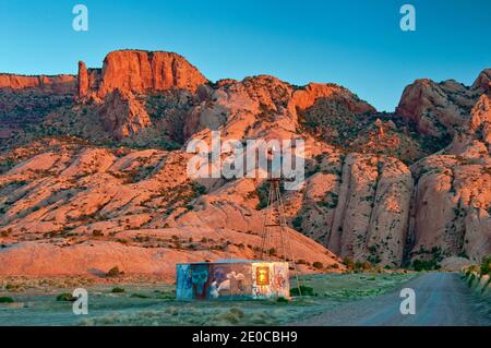 Mulino a vento e serbatoio d'acqua, Skeleton Mesa dietro, all'alba, Navajo Riserva indiana, vicino Kayenta, Arizona, Stati Uniti Foto Stock