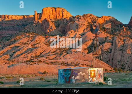 Mulino a vento e serbatoio d'acqua, Skeleton Mesa dietro, all'alba, Navajo Riserva indiana, vicino Kayenta, Arizona, Stati Uniti Foto Stock