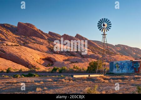 Mulino a vento e serbatoio d'acqua, Skeleton Mesa dietro, all'alba, Navajo Riserva indiana, vicino Kayenta, Arizona, Stati Uniti Foto Stock