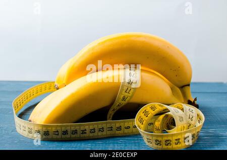 Banane e centimetro nastro è su uno sfondo di legno. Stile di vita sano. Cibo sano per perdita di peso Foto Stock