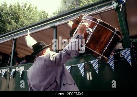 Germania/Baviera/ Chiemsee/uomo in abiti tradizionali che viaggiano in treno e il suo amico sta aiutando a caricare il suo grande tamburo attraverso la finestra del treno. Foto Stock