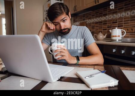 Lunedì mattina di nuovo. Il freelance insoddisfatto lavora a casa. Avendo la privazione di sonno, il ragazzo pigro millenario distratto dal lavoro si sente pigro mancanza di motivazione Foto Stock