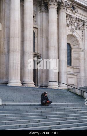 Londra, UK - Dicembre 2020 : una donna si siede sui gradini della Cattedrale di St Pauls, City of London Foto Stock