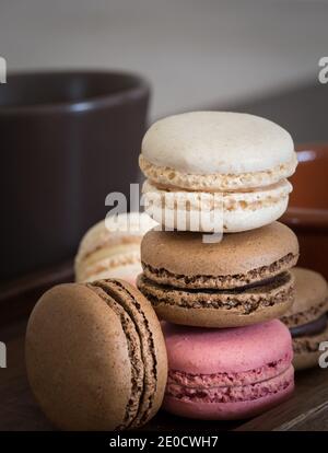 Un primo piano di una pila di macaron o Macaron colorati tra cui rosa, cioccolato e vaniglia con una tazza di caffè Foto Stock