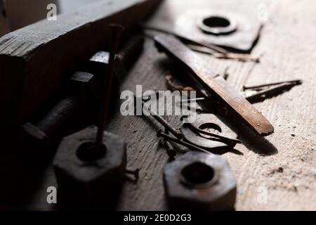 Dettaglio da officina abbandonata - chiodo, dispositivo di fissaggio e dado sporchi, arrugginiti e corrosi. Oggetti metallici e utensili sul legno. Messa a fuoco molto bassa. Foto Stock