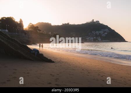 Una coppia gode l'ultimo po' di luce del sole in una passeggiata serale lungo la spiaggia di Ondaretta a San Sebastian, Spagna. Foto Stock
