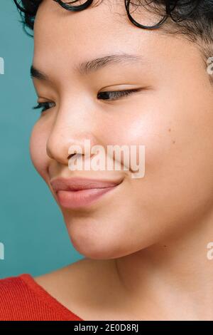 Ritratto della giovane Latina Donna con occhi asiatici che guardano di lato, primo piano, foto verticale isolata, sfondo verde acqua corrente Foto Stock