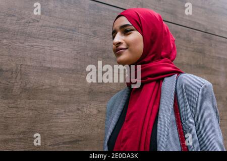 Contenuto giovane arabo femmina con abiti tradizionali hijab e casual camminando lungo la strada della città e guardando avanti Foto Stock