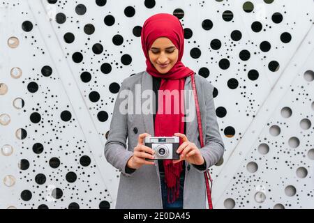 Arab femmina in rosso copricapo in piedi in città con retrò fotocamera e scatto di foto Foto Stock