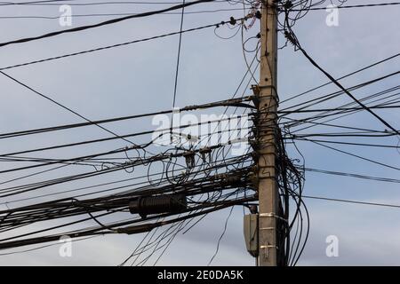 Palo elettrico con fili e cavi disordinati su cielo blu sfondo Foto Stock