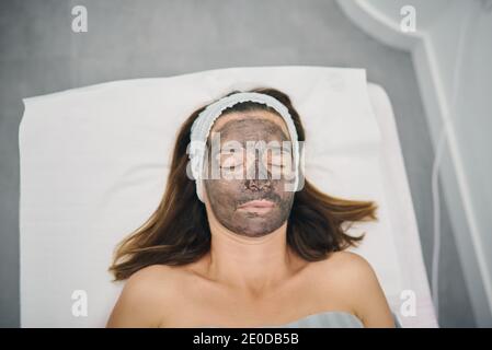 Da sopra cliente femminile con lozione di carbonio sulla preparazione del viso per la pelatura laser in un moderno centro di bellezza con gli occhi chiusi Foto Stock