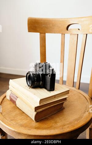 Fotocamera in vecchio stile posizionata su una pila di libri d'epoca su sgabello di legno in un luogo di lavoro creativo Foto Stock