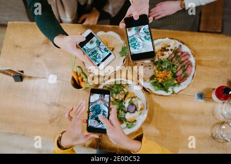 Dall'alto di diverse amici femminili che si riuniscono a tavola e. scattare foto di cibo sugli smartphone per i social media Foto Stock
