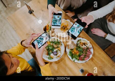 Dall'alto di diverse amici femminili che si riuniscono a tavola e. scattare foto di cibo sugli smartphone per i social media Foto Stock