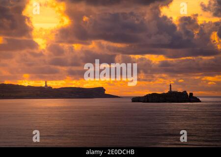 Pittoresco scenario di fari su scogliere rocciose in mare increspato Contro il cielo drammatico tramonto a Santander Foto Stock