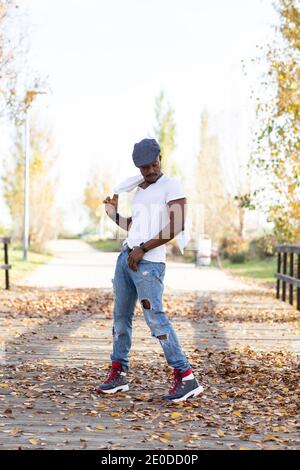 Bel maschio nero in abiti casual alla moda in piedi in autunno parcheggia e guarda lontano Foto Stock