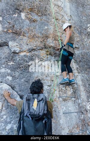 Basso angolo di alpinista attivo femmina che sale ripido roccioso pendenza di montagna mentre si allenano con istruttore maschile in natura Foto Stock