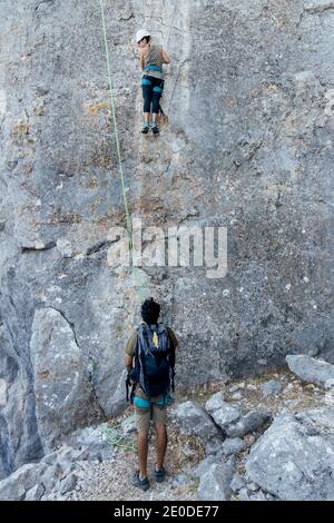 Basso angolo di alpinista attivo femmina che sale ripido roccioso pendenza di montagna mentre si allenano con istruttore maschile in natura Foto Stock