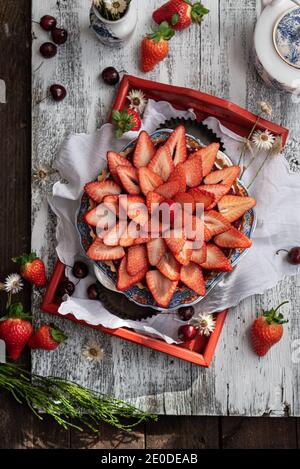 Dall'alto di crostata dolce decorata con fragole fresche servite su vassoio di legno su tavola con bacche assortite Foto Stock