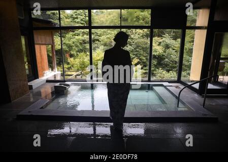 Giovane donna caucasica in un kimono che si prepara a godere. Un rilassante e tradizionale bagno termale acque termali in un onsen giapponese, vista da dietro Foto Stock