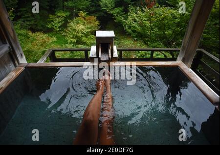 Gambe e piedi di una donna caucasica viaggiatore godendo di un bagno di acque termali in onsen giapponese, vista dall'alto Foto Stock