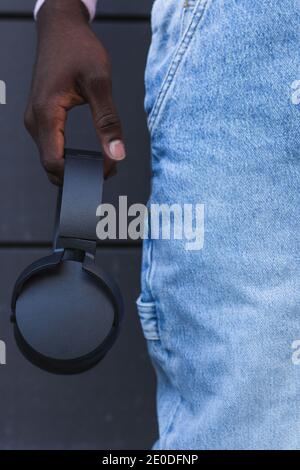 Irriconoscibile raccolto africano americano maschio in jeans in piedi con nero cuffie wireless in strada Foto Stock