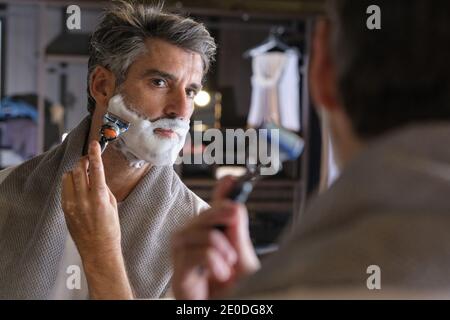 Per radere la barba, fate una foto dell'uomo di mezza età con i capelli grigi utilizzando una crema di rasatura. Foto Stock