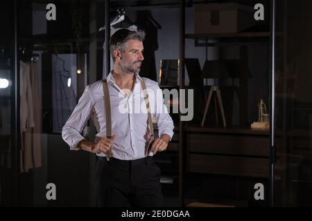 Foto d'inventario di un elegante uomo di mezza età che indossa abiti e sospensori sorridenti e che guarda di lato. Foto Stock