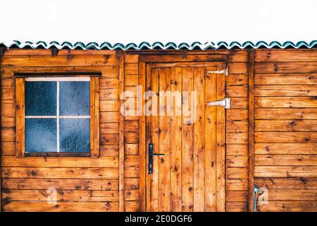 Accogliente tipica casa in legno con tetto innevato e piccola finestra coperto di brina il giorno d'inverno Foto Stock