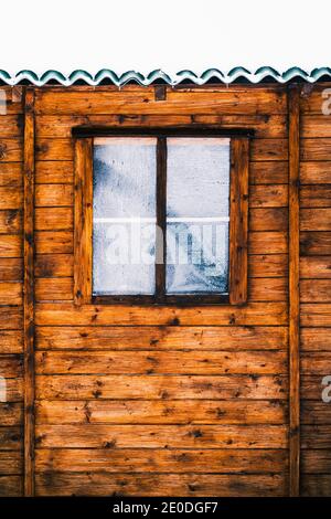 Accogliente tipica casa in legno con tetto innevato e piccola finestra coperto di brina il giorno d'inverno Foto Stock