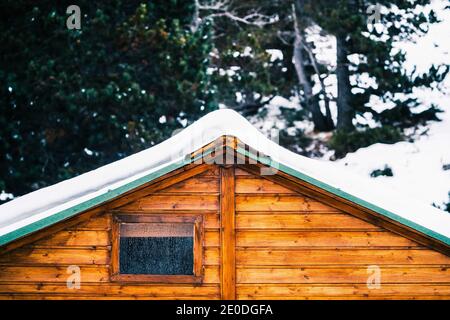 Accogliente tipica casa in legno con tetto innevato e piccola finestra coperto di brina il giorno d'inverno Foto Stock