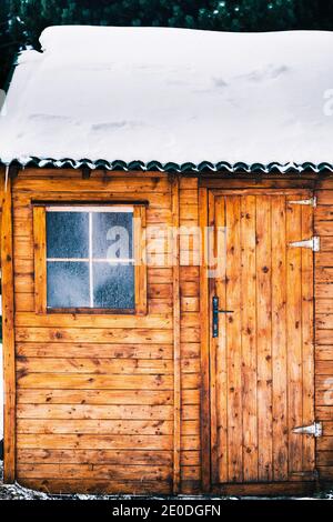 Accogliente tipica casa in legno con tetto innevato e piccola finestra coperto di brina il giorno d'inverno Foto Stock