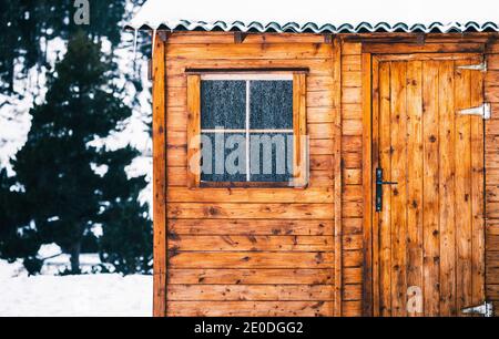 Accogliente tipica casa in legno con tetto innevato e piccola finestra coperto di brina il giorno d'inverno Foto Stock